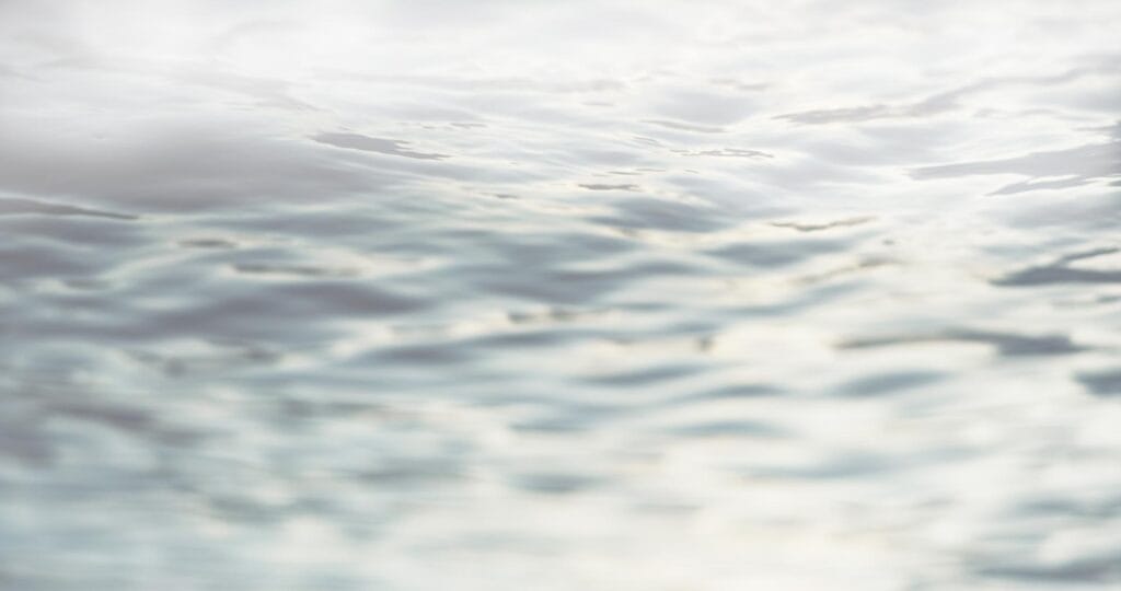Close-up view of gentle water ripples on a surface, with soft reflections and a light, slightly blurred appearance.