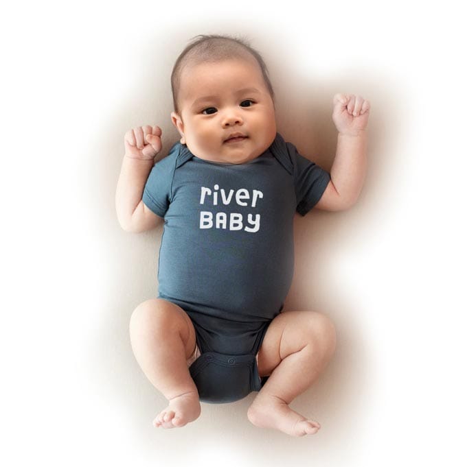 Baby lying down looking at camera wearing a onesie with "river baby" written on it